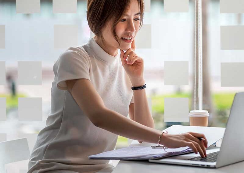 A woman smiling while working on a laptop, with a checkmark within a cogwheel icon representing book proofreading services.