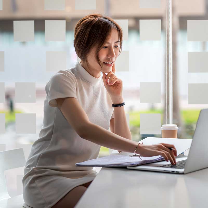 A woman smiling while working on a laptop, with a checkmark within a cogwheel icon representing book proofreading services.