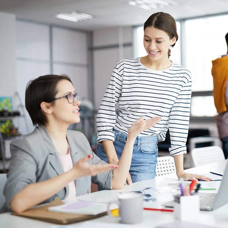 Two women collaborating on book editing, with a pencil icon indicating editing services.