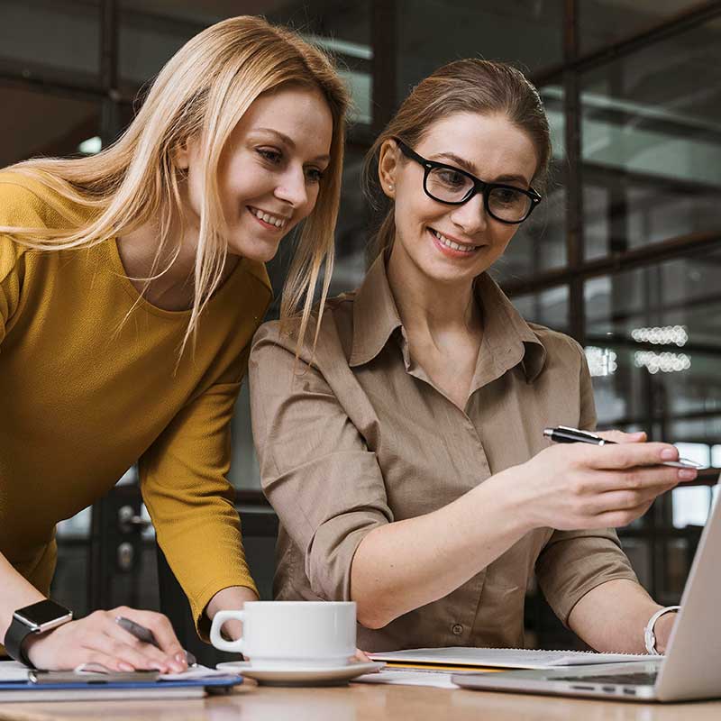 Two women looking at a tablet displaying an ebook, with a book icon symbolizing book publishing services.
