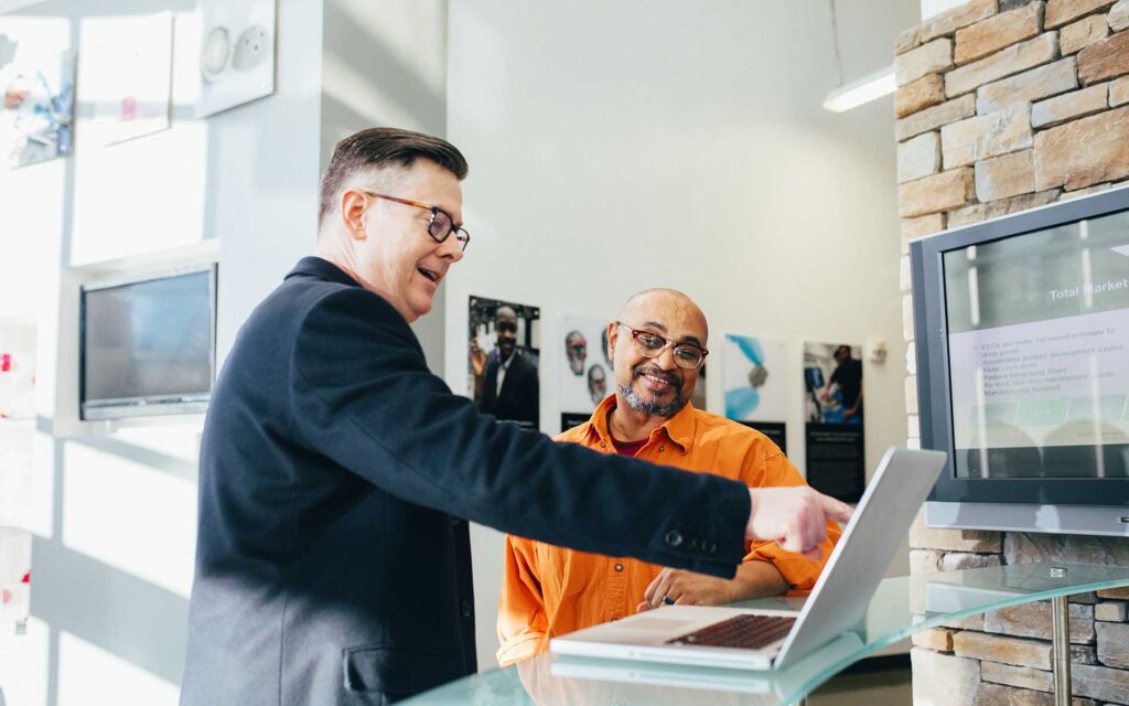 Two men looking at a laptop, possibly discussing publishing a book cost.