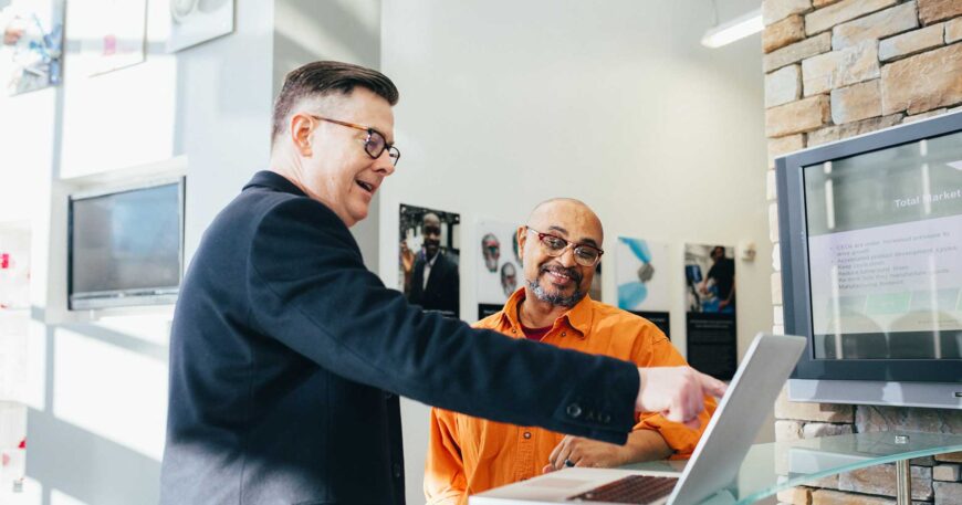 Two men looking at a laptop, possibly discussing publishing a book cost.