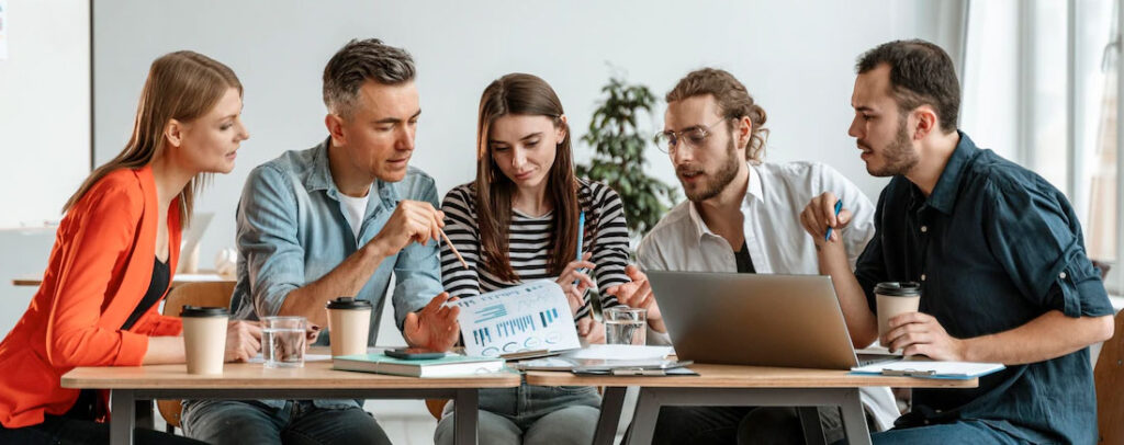 Three people collaborating over documents and a laptop, seemingly discussing strategies to publish a book on Amazon and make money.