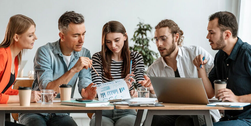 Three people collaborating over documents and a laptop, seemingly discussing strategies to publish a book on Amazon and make money.
