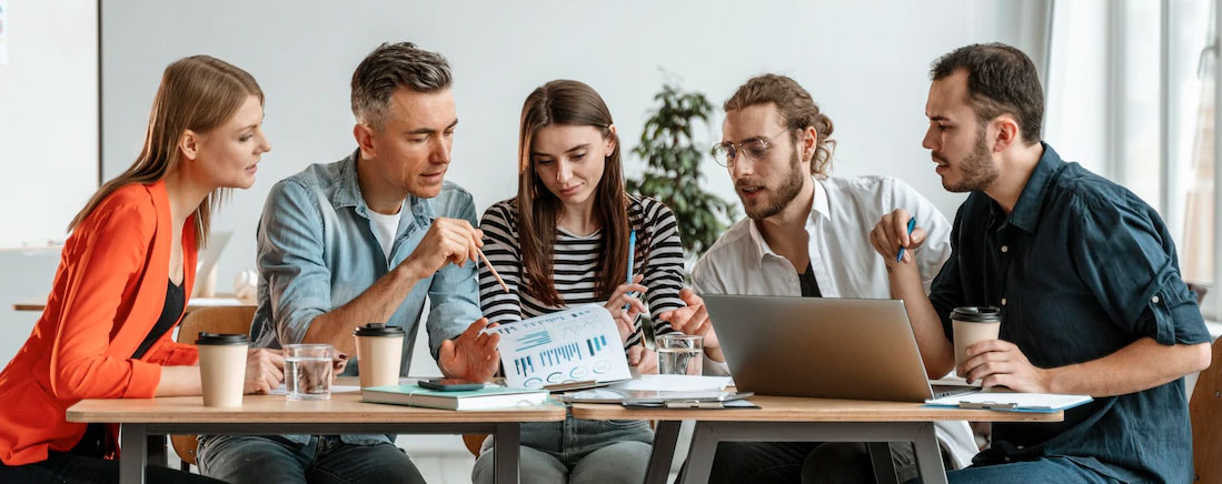 Three people collaborating over documents and a laptop, seemingly discussing strategies to publish a book on Amazon and make money.