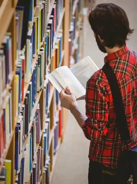 Person reading a book in a library, representing the research phase for self-publishing on Amazon.